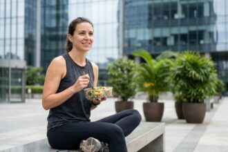 Femme active mangeant une salade saine en tenue de sport devant un immeuble de bureaux moderne pendant sa pause déjeuner