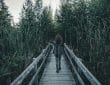 woman walking on wooden bridge between green grass during daytime