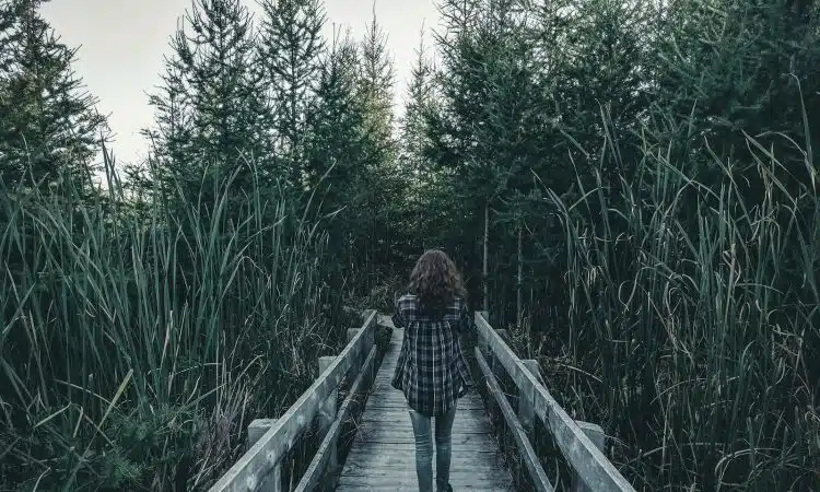 woman walking on wooden bridge between green grass during daytime